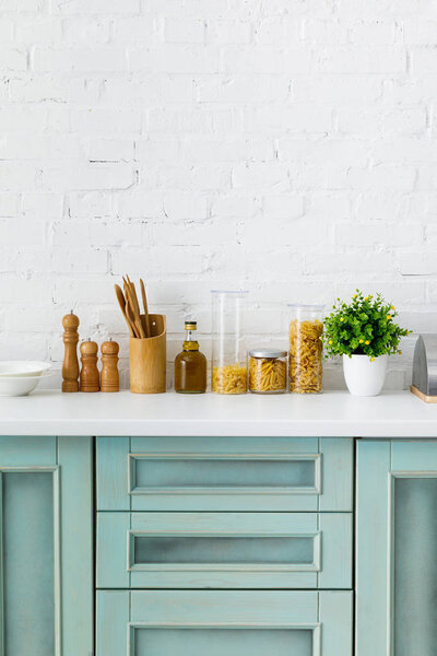 modern white and turquoise kitchen interior with kitchenware, food containers and plant near brick wall