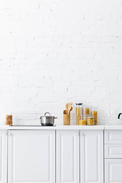 minimalistic modern white kitchen interior with kitchenware and food near brick wall