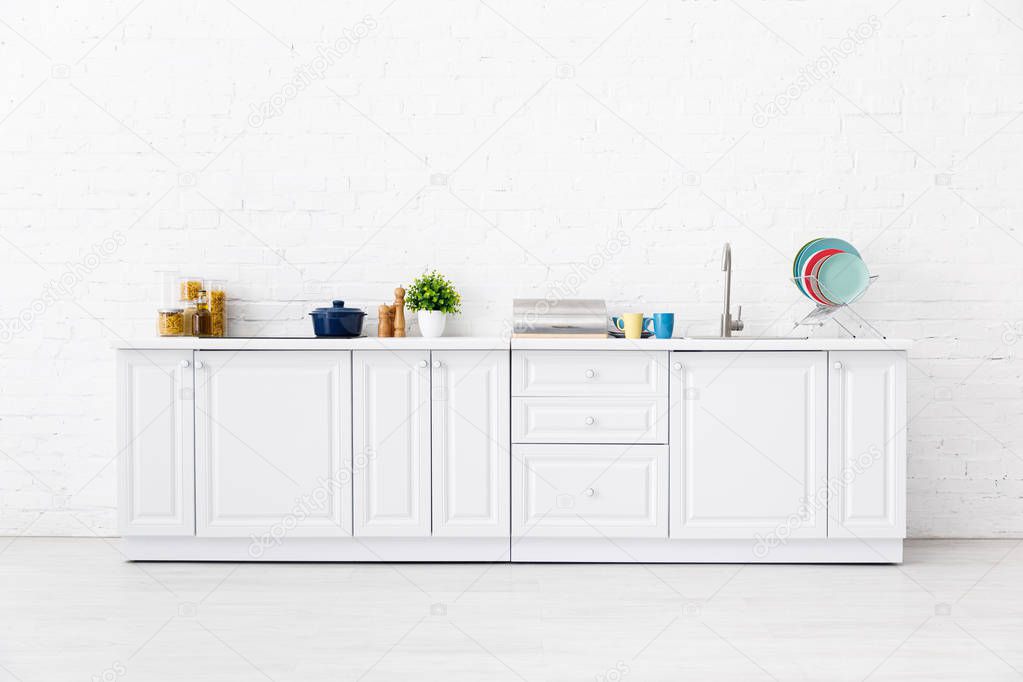 modern white kitchen interior with kitchenware near brick wall