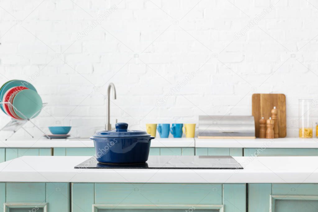 selective focus of modern white and turquoise kitchen interior with pot on electric induction cooktop