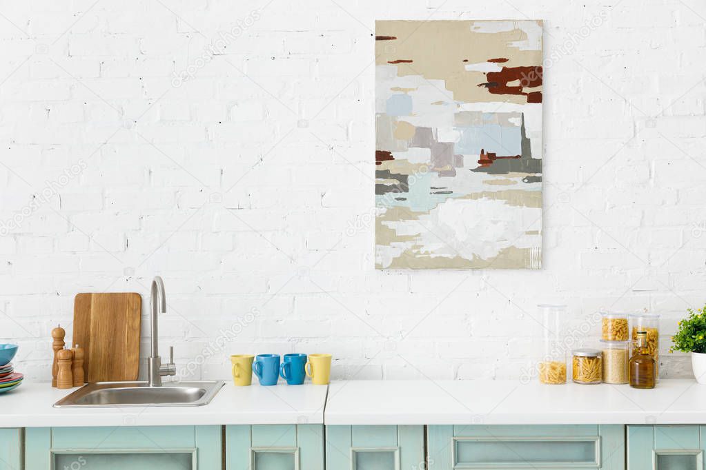 modern white and turquoise kitchen interior with kitchenware and abstract painting on brick wall