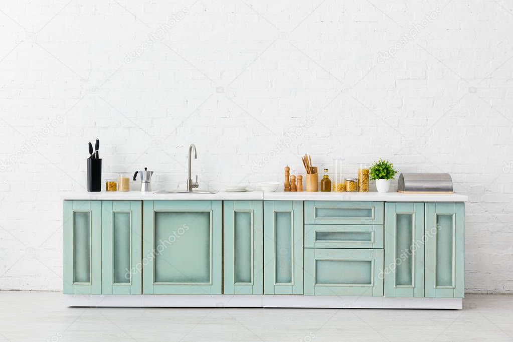 modern white and turquoise kitchen interior with kitchenware, food and sink near brick wall