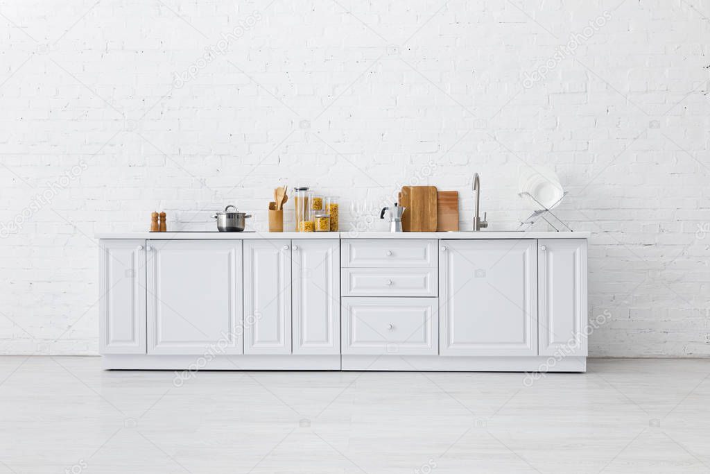 minimalistic modern white kitchen interior with kitchenware near brick wall