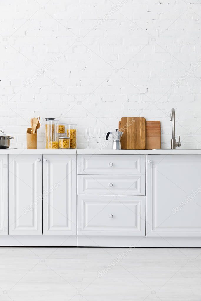 minimalistic modern white kitchen interior with kitchenware near brick wall