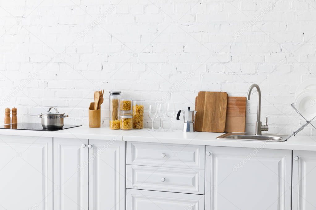 minimalistic modern white kitchen interior with kitchenware near brick wall