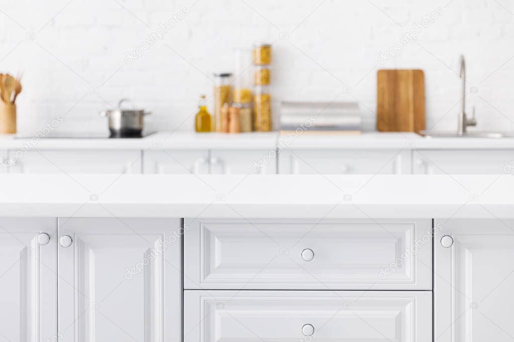 selective focus of empty tabletop and minimalistic modern white kitchen interior with kitchenware and food near brick wall on background