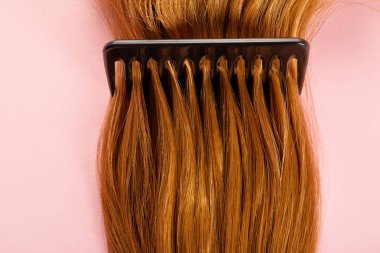 Pembe arka planda kahverengi saçlı tarağın üst görünümü