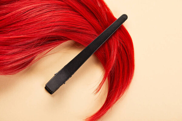 Top view of clip and colored red hair on beige background