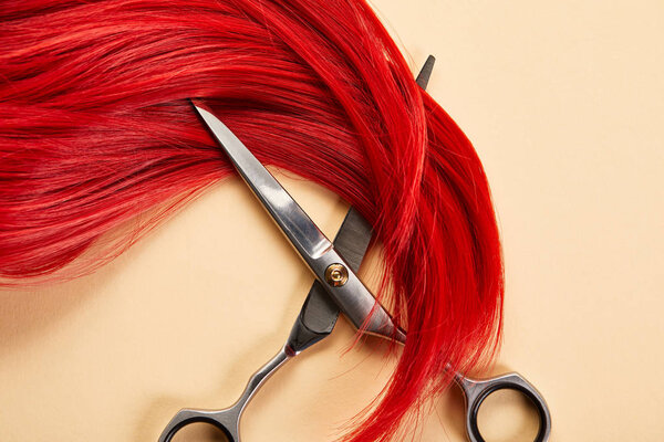 Top view of red hair and scissors on beige background