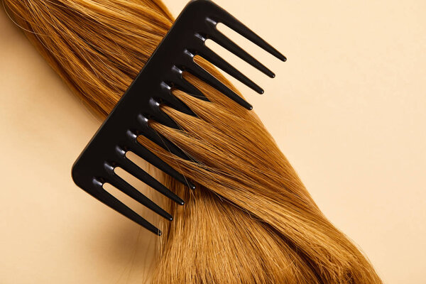 Top view of comb in twisted brown hair on beige background