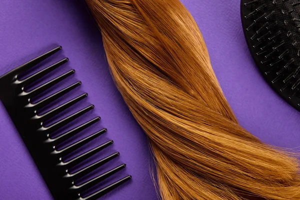 紫色背景的带有梳子和梳子的棕色头发的顶部视图 — 图库照片