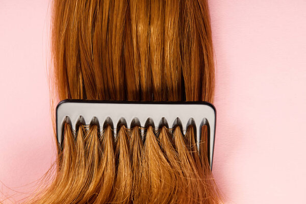 Top view of comb in brown hair on pink background