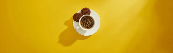 黄色の表面にソーサーでクッキーとコーヒーカップのトップビュー パノラマショット — ストック写真