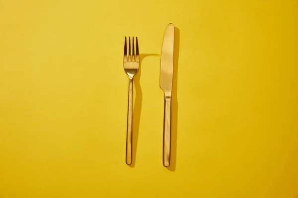 コピースペースと黄色の背景に光沢のあるフォークとナイフのトップビュー — ストック写真