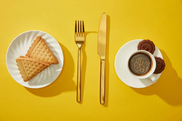 带咖啡杯和黄色背景饼干的金色餐具的顶部视图 — 图库照片