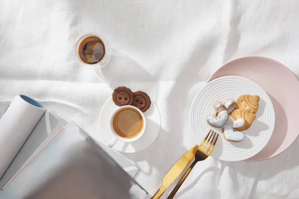 新鮮なコーヒーのトップビュー 白いテーブルクロスの釉薬と雑誌とクッキー — ストック写真