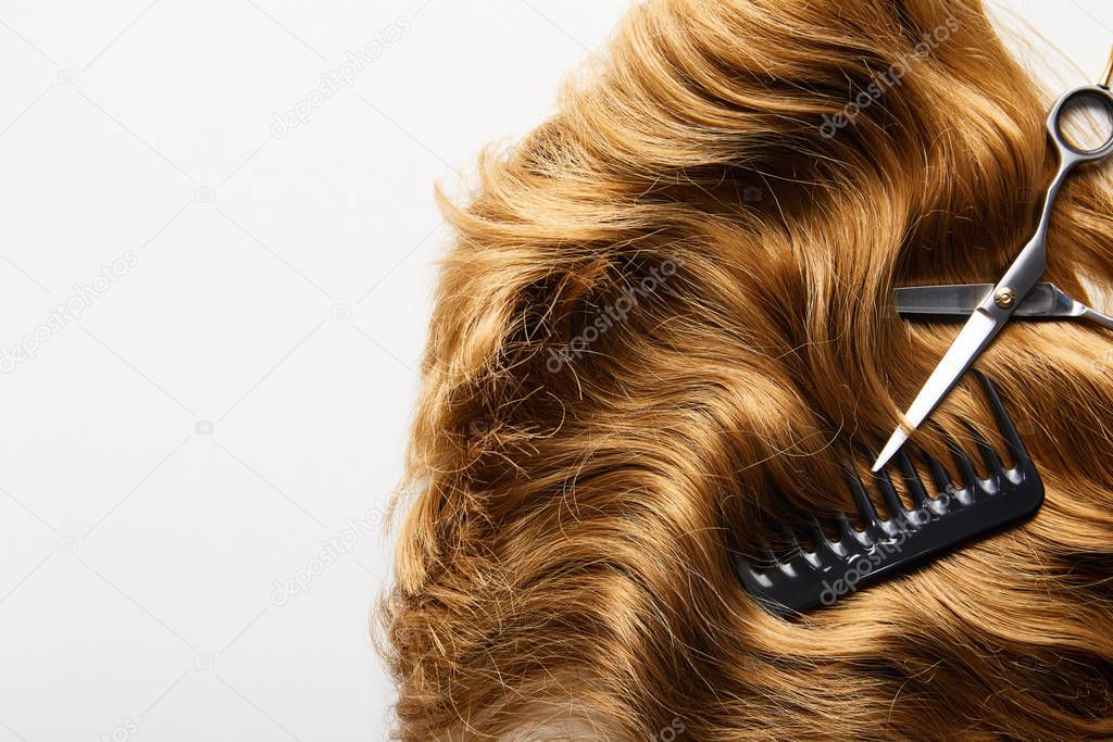 Top view of scissors and comb on brown hair isolated on white