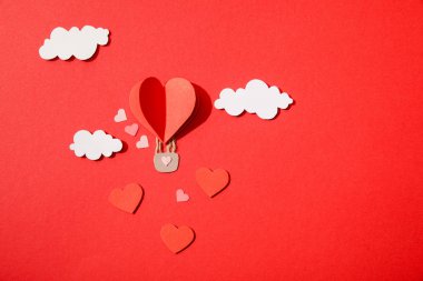 Kağıt kalp şeklindeki hava balonunun üst görüntüsü kırmızı arkaplanda bulutlarda