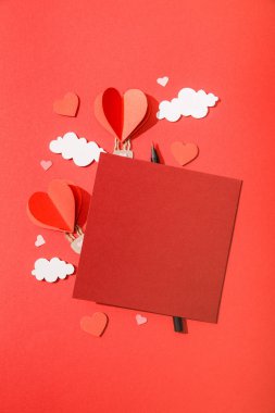 top view of paper heart shaped air balloons in clouds near blank card and pencil on red background clipart