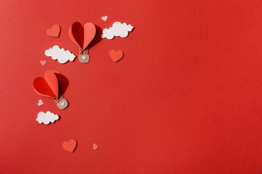 Kağıt kalbin üst görüntüsü kırmızı arkaplanda bulutların içindeki hava balonları şekillendirdi
