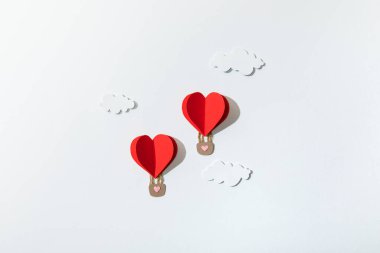 Kağıt kalbin üst görüntüsü beyaz arkaplanda bulutlarda hava balonları şeklinde.