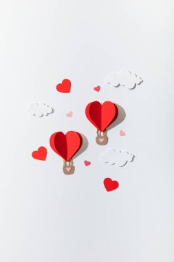Kağıt kalbin üst görüntüsü beyaz arkaplanda bulutlarda hava balonları şeklinde.