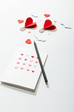 Kağıt kalp yakınındaki kalpler ve kalemle dolu tebrik kartının seçici odak noktası beyaz arkaplandaki bulutlarda hava balonları şeklinde.