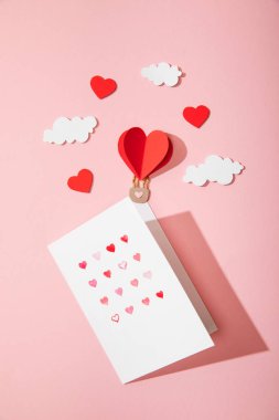 Tebrik kartının en üst görüntüsü beyaz zarfın içinde kalpler kağıt kalp şeklinde hava balonu şeklinde pembe bulutlar üzerinde