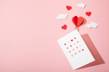 Tebrik kartının en üst görüntüsü beyaz zarfın içinde kalpler kağıt kalp şeklinde hava balonu şeklinde pembe bulutlar üzerinde