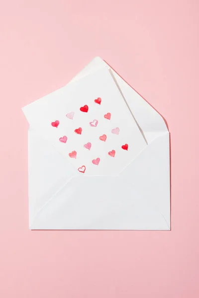 ピンクに隔離された白い封筒にハートのグリーティングカードのトップビュー — ストック写真