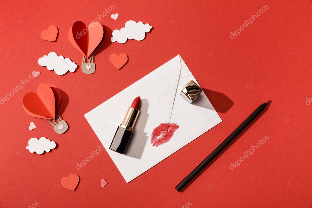 top view of paper clouds and heart shaped air balloons, envelope with lip print, lipstick and pencil on red background