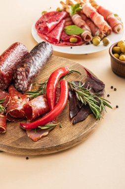 Zeytin, baharat ve ekmek çubuklarıyla servis edilen lezzetli et tabakları ve bej arka planda ahşap tahta tabaklar.