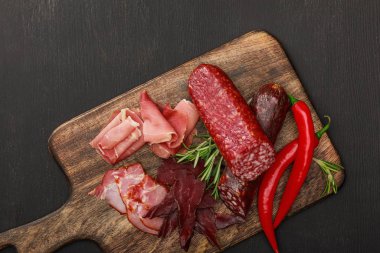 top view of delicious meat platter served with chili pepper and rosemary on wooden black table clipart