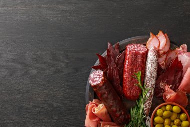 Ahşap masa üzerinde zeytin ve otlarla servis edilen lezzetli et tabağının üst görüntüsü.