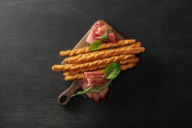 Tahta masa üzerinde ekmek çubukları ve otlarla servis edilen lezzetli et tabağının üst görüntüsü.