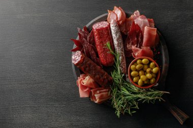 Ahşap masa üzerinde zeytin ve otlarla servis edilen lezzetli et tabağının üst görüntüsü.
