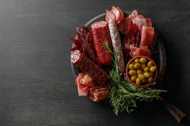 top view of delicious meat platter served with olives and herbs on wooden black table clipart