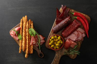 Tahta üzerinde zeytin, ekmek ve otlarla servis edilen lezzetli et tabaklarının üst görüntüsü.