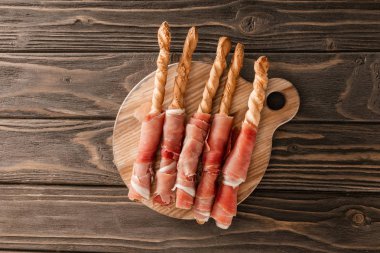top view of delicious meat platter with breadsticks and prosciutto on wooden board clipart