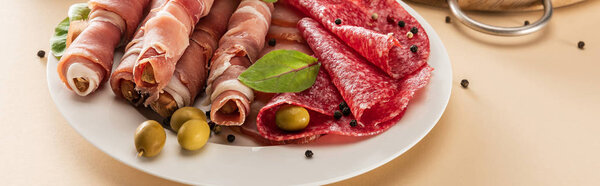 вкусное мясное блюдо подается с оливками и хлебными палочками на тарелке на бежевом фоне, панорамный снимок
