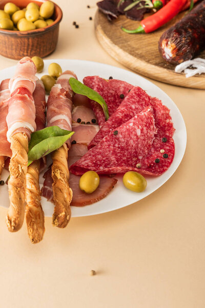 delicious meat platters served with olives, spices and breadsticks on plate and wooden board on beige background