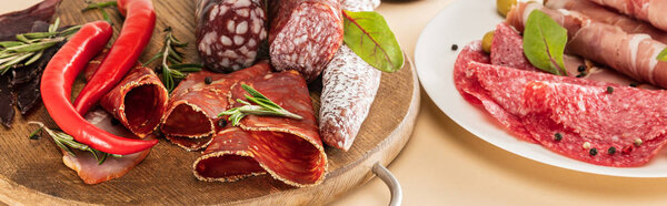 delicious meat platters served with olives, spices on plate and wooden board on beige background, panoramic shot