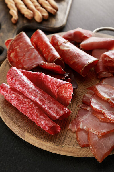 delicious meat platter on wooden board on black surface