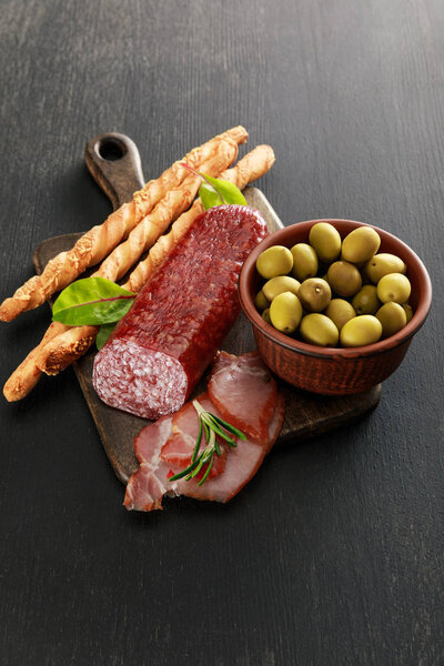 delicious meat platter served with olives and grissini on board on black surface