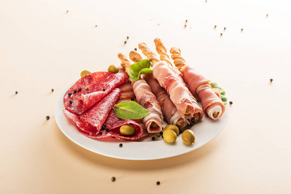 вкусное мясное блюдо подается с оливками и хлебными палочками на тарелке на бежевом фоне
