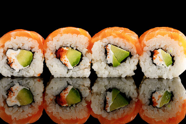fresh delicious Philadelphia sushi with avocado, creamy cheese, salmon and masago caviar isolated on black with reflection