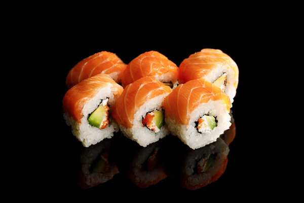 delicious Philadelphia sushi with avocado, creamy cheese, salmon and masago caviar isolated on black