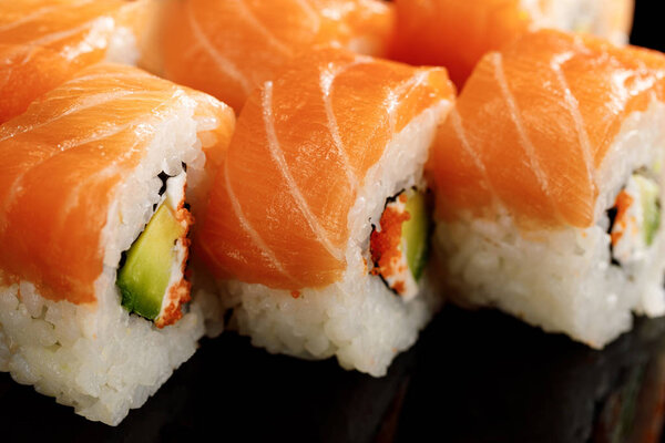 закрытый вид на вкусные суши Филадельфии с авокадо, сливочный сыр, лосось и икра мазаго изолированы на черном
