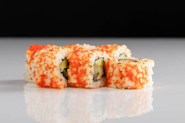 delicious California roll with avocado, salmon and masago caviar on white surface isolated on black