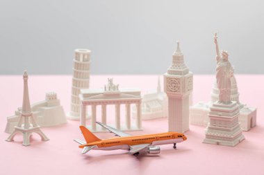 toy airplane near small statuettes of different countries on grey and pink  clipart
